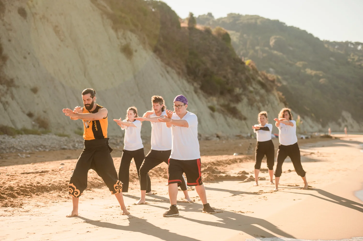 Group practising Kung Fu stances together on the beach in golden evening light