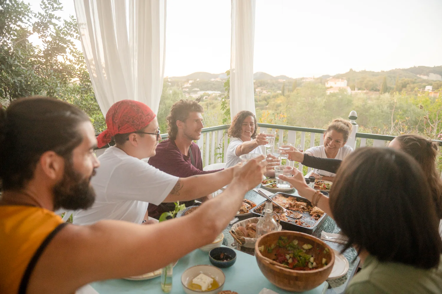 Group sharing a meal together on a terrace overlooking the Corfu countryside at sunset