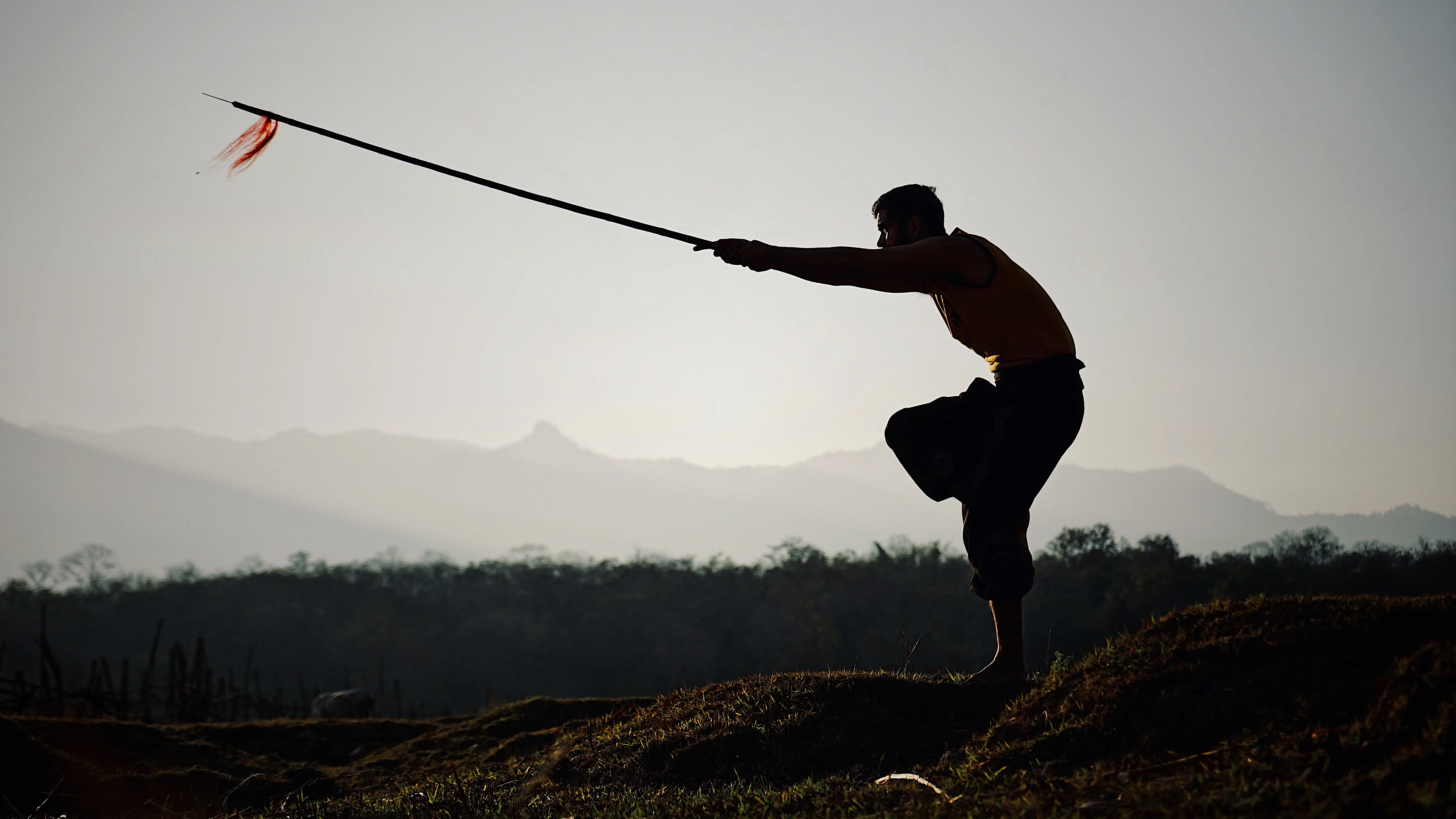 Silhouette of Thomas practising with a spear at dusk