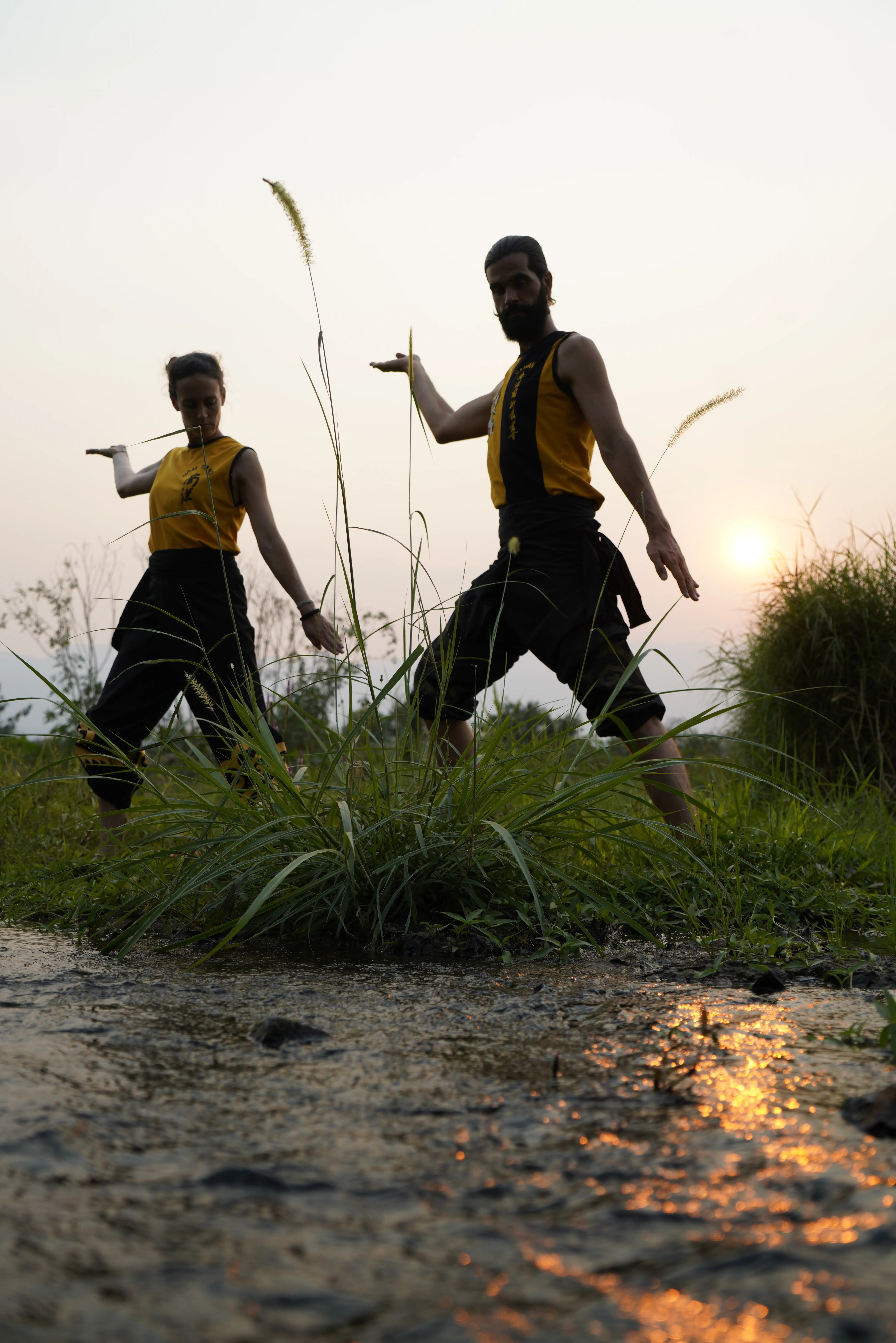 Two practitioners performing Shuang Yang beside the water at sunrise in Thailand, calm and flowing atmosphere