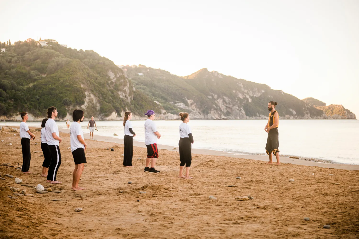 Thomas leading a group class on Arillas beach with the sea and coastline visible in the background